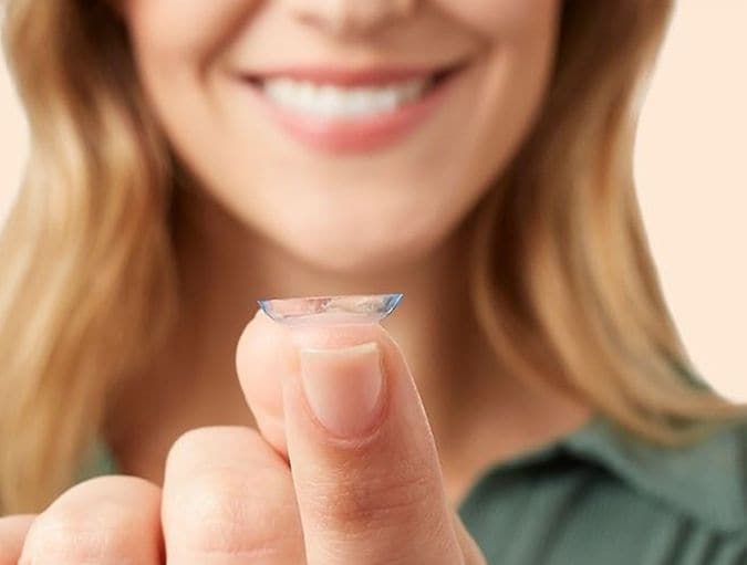 Een vrouw glimlacht terwijl ze naar een contactlens op haar vinger kijkt.