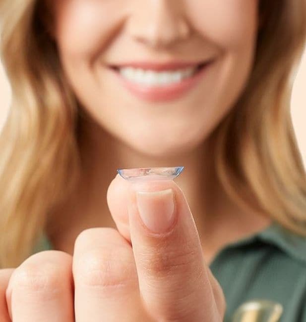 Een vrouw glimlacht terwijl ze naar een contactlens op haar vinger kijkt. 